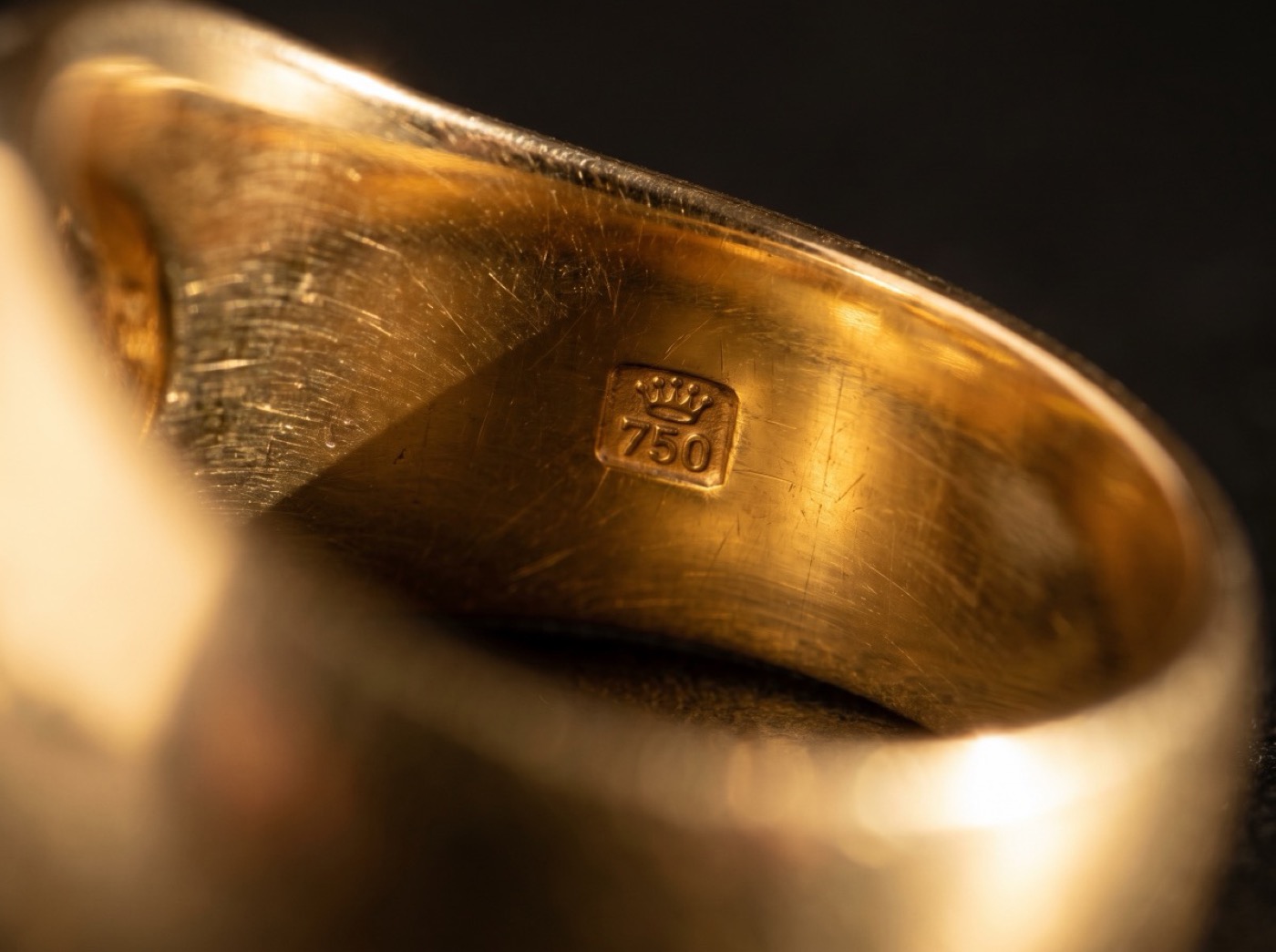 A macro photograph of a 750 hallmark stamped inside a gold ring band.
